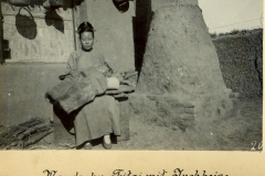 Eine Mandschu Taitai sitzt mit Tuchheise vor einem traditionellen Haus in China und lebt ihren Alltag