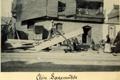 Chinesische Sägemühle in einer historischen Stadt in China, wo ein Arbeiter Holz zuschneidet und andere Personen zuschauen