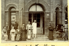 Historische Aufnahme japanischer Kaufleute in China vor einem Geschäft in einer urbanen Szenerie des frühen 20. Jahrhunderts