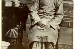 Ein chinesisches Mädchen in traditioneller Kleidung sitzt in einem Raum mit antiken Möbeln und einer Uhr auf dem Tisch