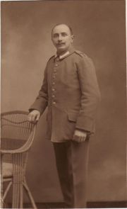 Ein Soldat in Uniform steht an einem Stuhl in einem Studio von 1910
