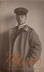 Ein historischer Soldat in Uniform mit einem Mantel und Mütze vor einer Wand