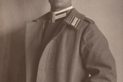 Ein historischer Soldat in Uniform mit einem Mantel und Mütze vor einer Wand