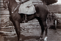 Ein Soldat auf einem Pferd vor einem Holzgebäude in ländlicher Umgebung