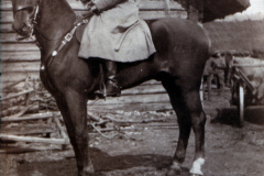Ein Soldat auf einem Pferd vor einem Holzgebäude in ländlicher Umgebung