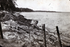 Mann am Ufer eines Gewässers mit Drahtzaun in der Natur