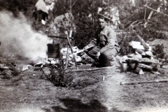Ein Mann sitzt im Wald und kocht über einem Lagerfeuer