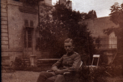 Junger Soldat sitzt auf einem Stuhl in einem Garten vor einem alten Gebäude