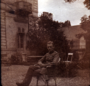 Junger Soldat sitzt auf einem Stuhl in einem Garten vor einem alten Gebäude