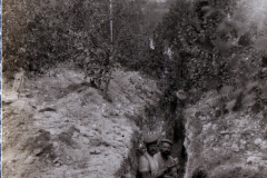 Zwei Soldaten stehen in einem Schützengraben, umgeben von Erde und Vegetation
