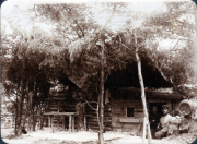 Ein historisches Blockhaus in der Natur mit Personen im Hintergrund