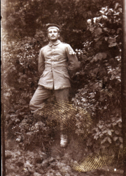 Ein Soldat in Uniform steht vor einer grünen Wand aus Pflanzen im Freien
