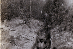 Zwei Soldaten stehen in einem Schützengraben, umgeben von Erde und Vegetation