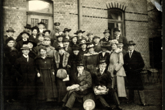 Gruppenaufnahme von Männern und Frauen in historischen Outfits vor einem Backsteingebäude