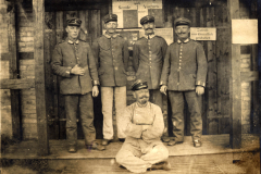 Fünf Soldaten stehen vor einem Holzgebäude, während ein weiterer sitzt und an der Zeitreise teilnimmt
