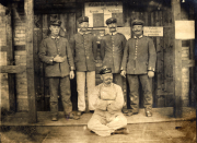 Fünf Soldaten stehen vor einem Holzgebäude, während ein weiterer sitzt und an der Zeitreise teilnimmt