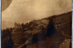 Bergdorf im Nebel mit historischen Gebäuden und Wald umgeben, auf einem sanften Hang in den Alpen