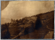 Bergdorf im Nebel mit historischen Gebäuden und Wald umgeben, auf einem sanften Hang in den Alpen