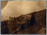 Bergdorf im Nebel mit historischen Gebäuden und Wald umgeben, auf einem sanften Hang in den Alpen