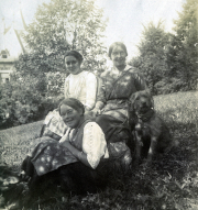 Drei Frauen in traditioneller Kleidung posieren mit Hunden im Freien in einer ländlichen Umgebung