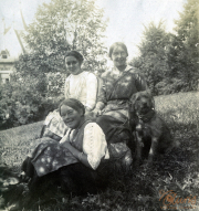 Drei Frauen in traditioneller Kleidung posieren mit Hunden im Freien in einer ländlichen Umgebung