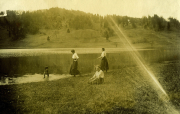 Darstellung einer ländlichen Szene mit mehreren Personen am Ufer eines ruhigen Gewässers in den frühen 1900er Jahren