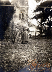 Frau im Garten steht mit einem Kind, umgeben von Bäumen und einem Gebäude, in einer historischen schwarz-weiß Aufnahme