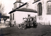 Ein historischer Moment mit einem Krankenwagen vor einer Kirche in ländlicher Umgebung