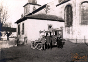 Ein historischer Moment mit einem Krankenwagen vor einer Kirche in ländlicher Umgebung