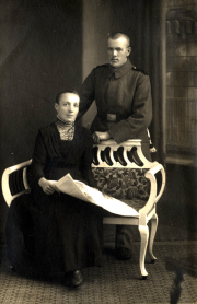 Portrait eines Soldaten in Uniform mit einer Frau auf einem Sofa vor neutralem Hintergrund in einem historischen Setting