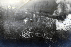 Historische Bahnhofsanlage mit dampfbetriebenem Zug und Arbeiter im Schatten von Bäumen