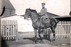 Heer-Offizier im Uniform reitet auf einem Pferd vor einem Stall in ländlicher Umgebung