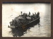 Auf einem Fluss wird ein Schiff mit militärischem Gerät und Soldaten beladen. Die Szene zeigt Waggons und Kanonen, während sich eine Gruppe von Männern beim Verladen beschäftigt. Der Zeitpunkt dieser Aufnahme könnte im Jahr 1916 liegen.