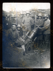 In einem Feldgraben stehen mehrere Soldaten der Heer, S.M.W. Zug 48 P.B. 11. Sie umgeben ein großes Geschütz und posieren während einer kurzen Unterbrechung des Dienstes. Die Szenerie zeigt den rauen Alltag im Ersten Weltkrieg.