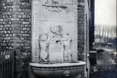 Steinerner Wandbrunnen mit Wappen und Reliefverzierung an Backsteinmauer