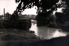 Flusslandschaft mit Ortschaft und Industriegebäuden im Hintergrund