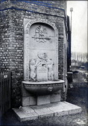 Steinerner Wandbrunnen mit Wappen und Reliefverzierung an Backsteinmauer