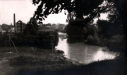 Flusslandschaft mit Ortschaft und Industriegebäuden im Hintergrund