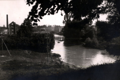 Flusslandschaft mit Ortschaft und Industriegebäuden im Hintergrund