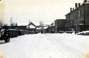 Verschneite Dorfstraße mit mehrstöckigen Gebäuden und Kirchturm im Winter