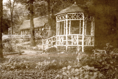 Hölzerner Pavillon mit ornamentalen Verzierungen in bewaldeter Umgebung