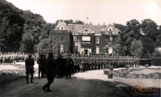 Militärparade vor einer beeindruckenden Residenz inmitten üppiger Vegetation und historischem Ambiente