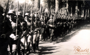Soldaten marschieren in geordneter Formation entlang einer von Bäumen gesäumten Straße