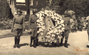 Männer in Uniform tragen einen goldenen Kranz bei einer Zeremonie in einer historischen Umgebung