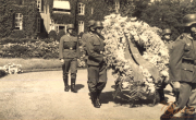 Soldaten bei einer feierlichen Zeremonie mit einer prachtvollen Blumenkranztrage inmitten historischer Architektur