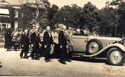 Historische Versammlung vor einem eleganten Automobil in ruhiger, parkähnlicher Umgebung