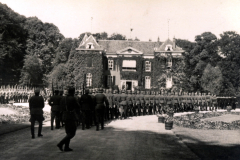 Militärparade vor einer beeindruckenden Residenz inmitten üppiger Vegetation und historischem Ambiente