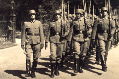 Soldaten in Uniform marschieren stolz durch einen Park im Sommer mit historischen Waffen
