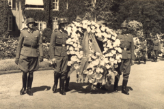 Männer in Uniform tragen einen goldenen Kranz bei einer Zeremonie in einer historischen Umgebung