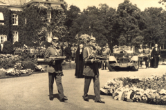 Historische Zeremonie mit uniformierten Offizieren und festlichem Empfang in einer malerischen Gartenanlage im 20. Jahrhundert